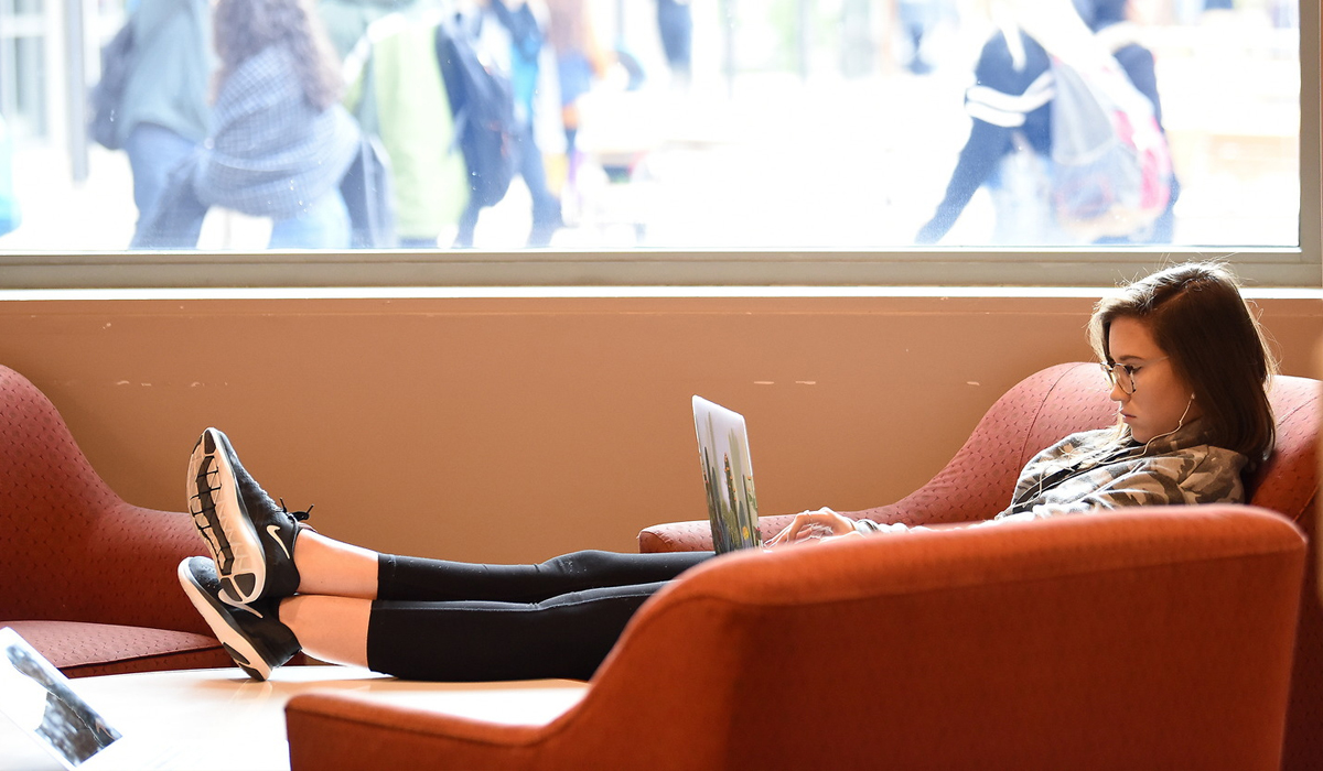 Female student studying and reading with legs up on sofa