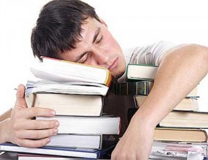 Male student sleeping on a pile of book